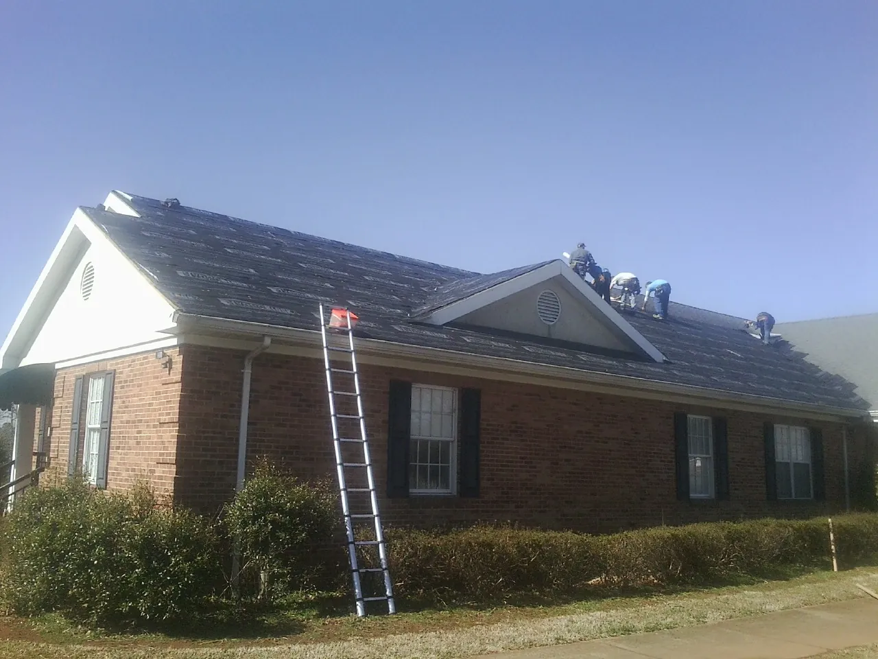 Crew tearing shingles off a brick ranch roof with a ladder set — Emergency Roof Repair work by our crew in Montgomeryville