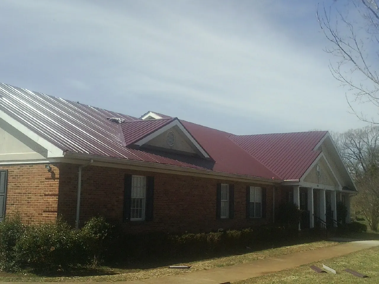 Red metal roof with gabled entries on a long brick building, from a Hail Damage Roof Repair job in Montgomeryville