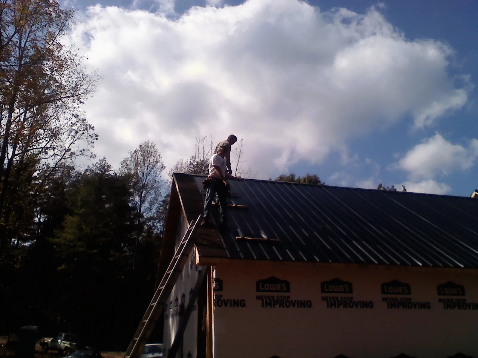 Roofer fastening dark metal panels high against a cloudy sky, from a Roof Inspection job in Montgomeryville