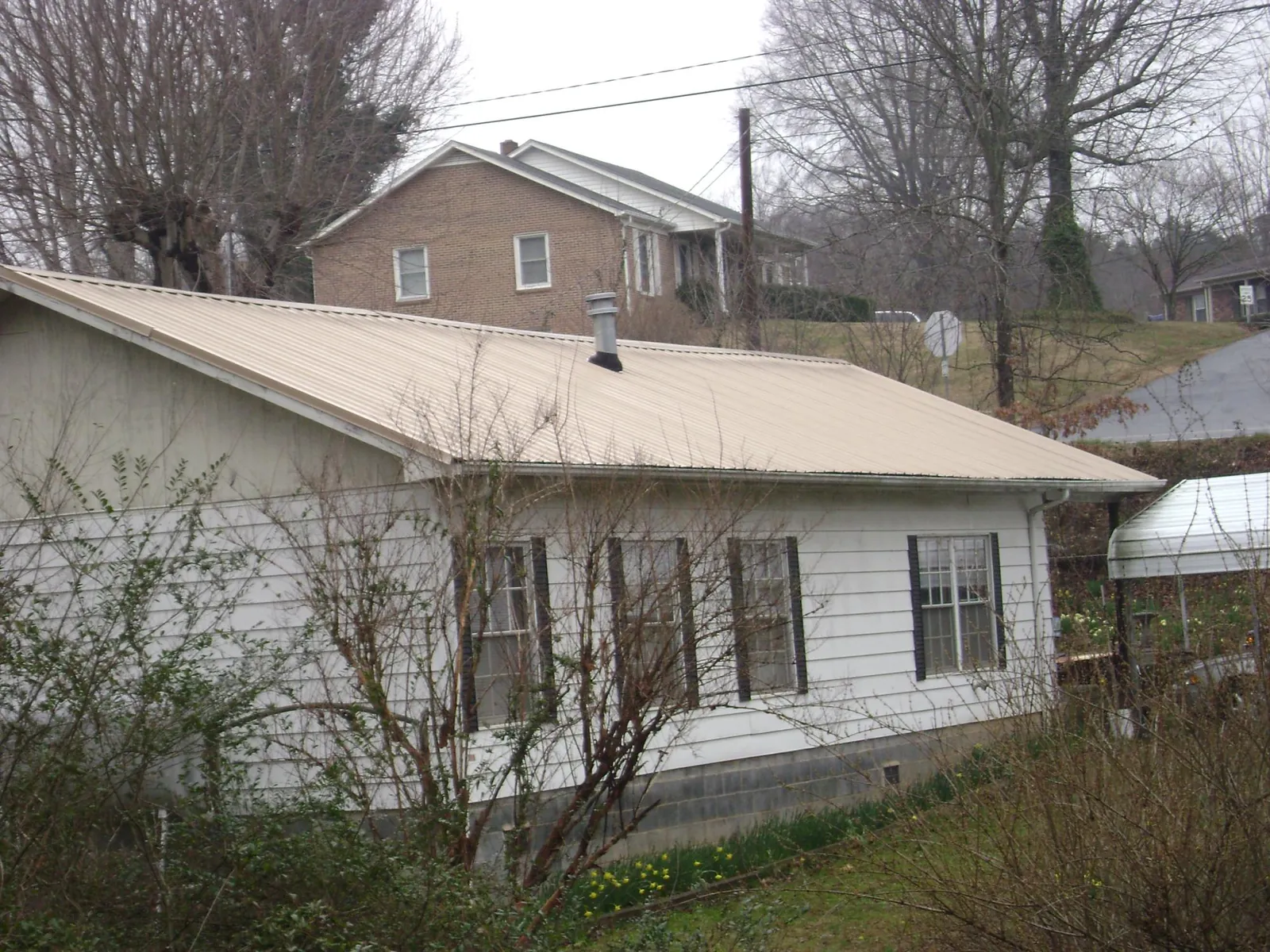 Tan metal roof on a white sided house set into a hillside — Commercial Roofing by Roofing Brothers in Montgomeryville